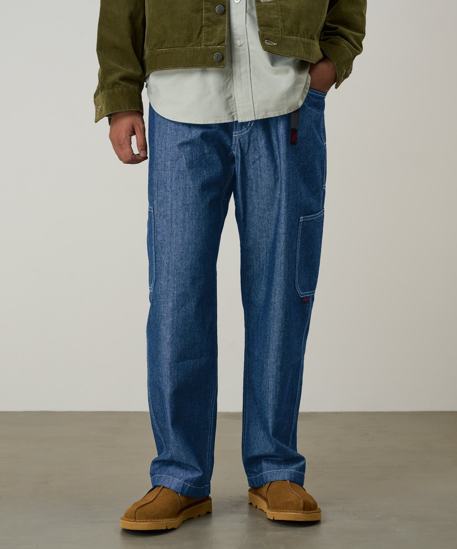 Model wearing blue Japanese Chambray Rock Slide Pant and a moss green jacket on a light-tone background.