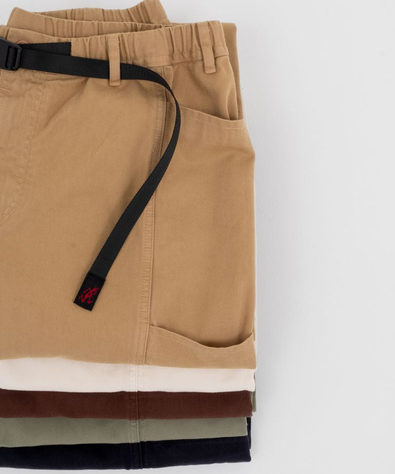 Several folded Gramicci Gadget Pants in various colors with a black belt on a white background