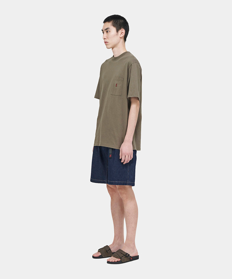 Model wearing a coyote brown Gramicci One Point Tee with a small running man graphic and blue shorts on a light-tone background.