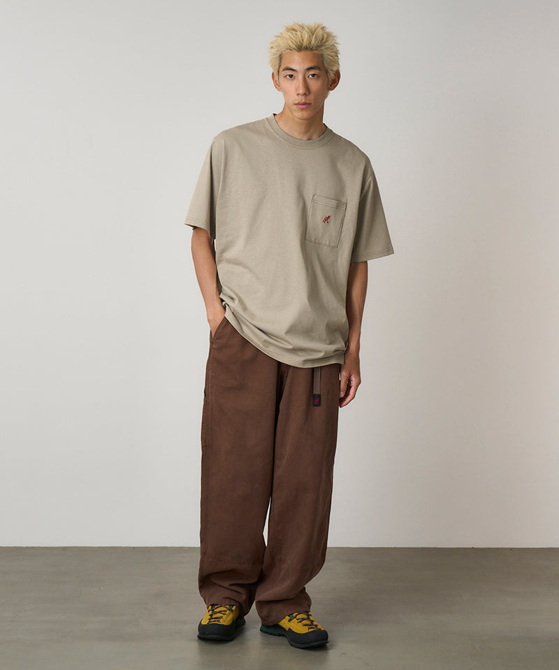 Model wearing a beige Gramicci One Point Tee with a small running man graphic and brown pants on a light-tone background.