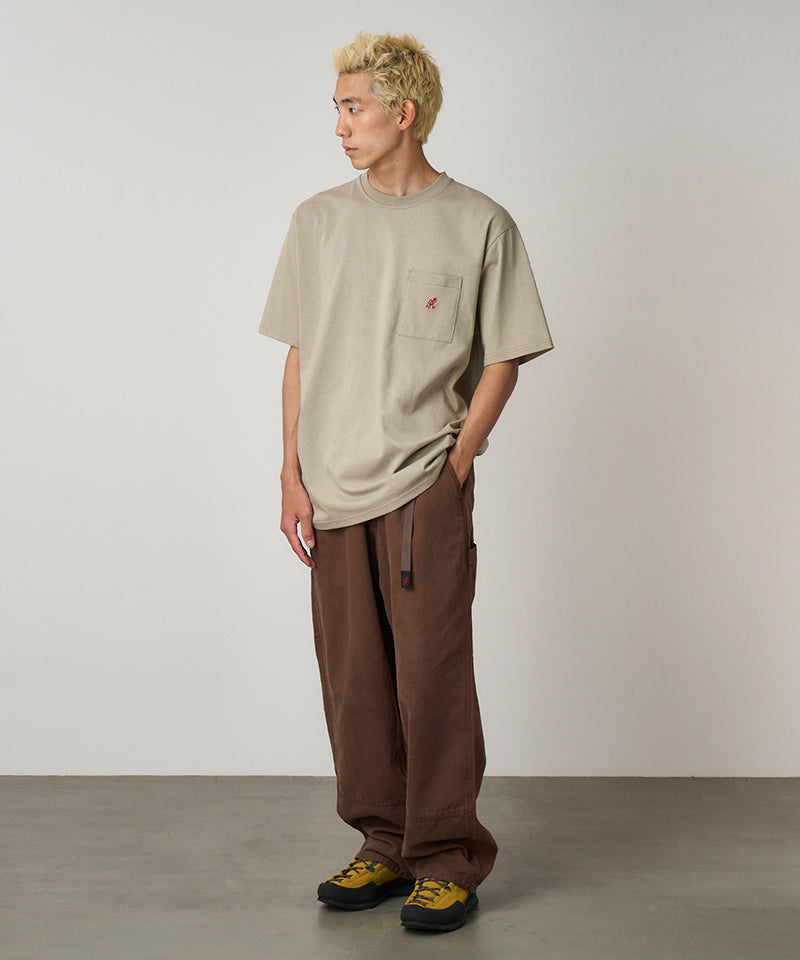 Model wearing a beige Gramicci One Point Tee with a small running man graphic and brown pants on a light-tone background.