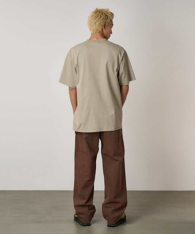 Back view of a model wearing a beige Gramicci One Point Tee and brown pants on a light-tone background.