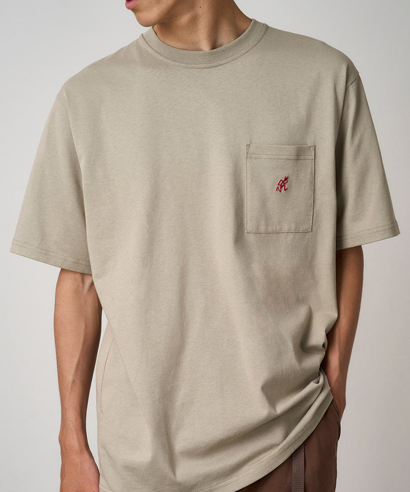 Model wearing a Gramicci beige One Point Tee with a small running man graphic against a light-tone background.