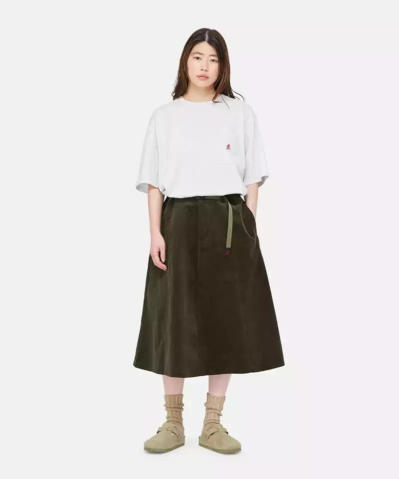 Model wearing a grey heather Gramicci One Point Tee with a small running man graphic and olive skirt on a light-tone background.