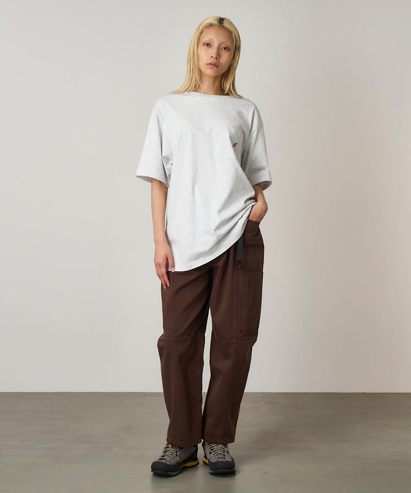 Model wearing a heather ash Gramicci One Point Tee with a small running man graphic and brown pants on a light-tone background.