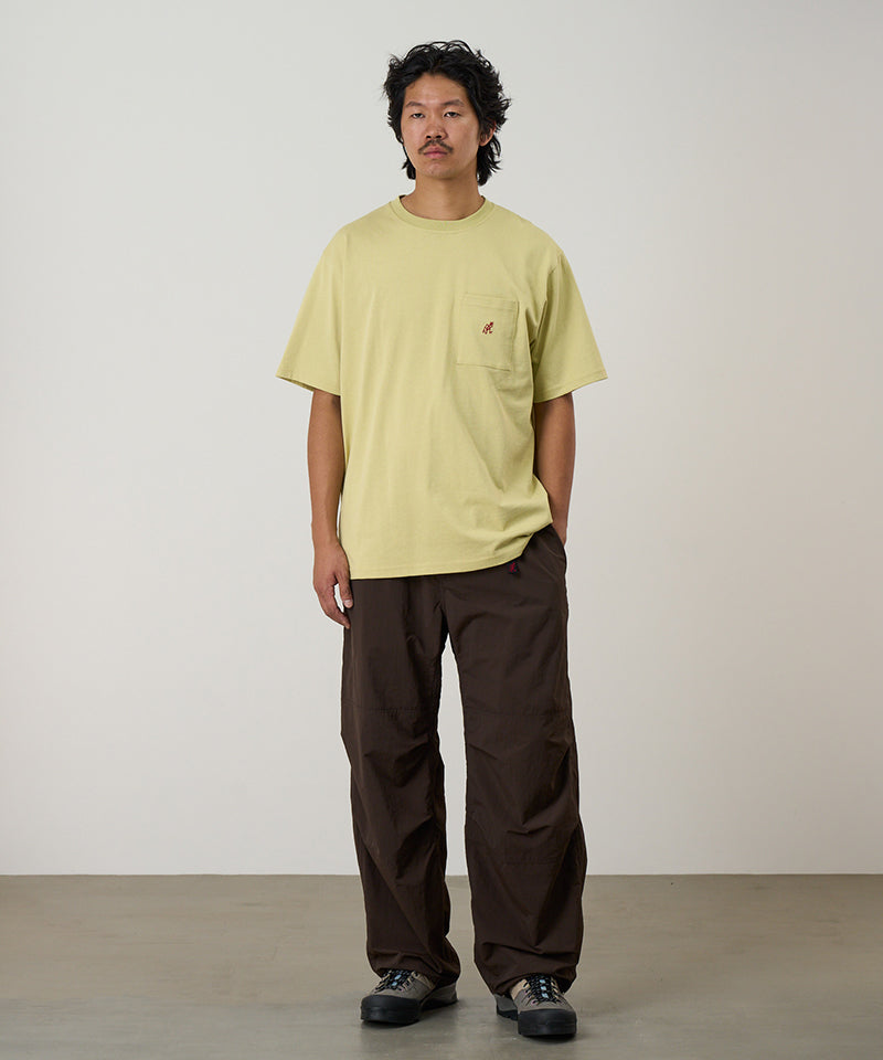 Model wearing a lime green
Gramicci One Point Tee with a small running man graphic and brown pants on a light-tone background.
