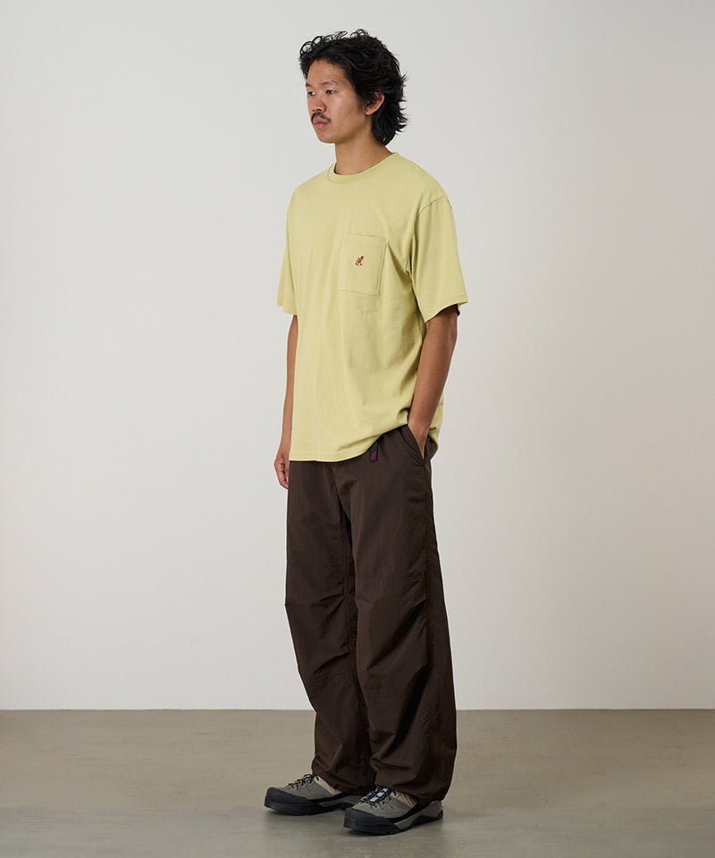 Model wearing a lime green Gramicci One Point Tee with a small running man graphic and brown pants on a light-tone background.