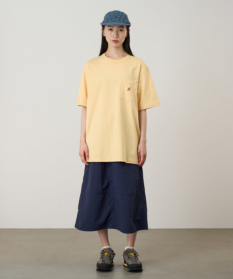 Model wearing a mango colored Gramicci One Point Tee with a small running man graphic and blue skirt on a light-tone background.