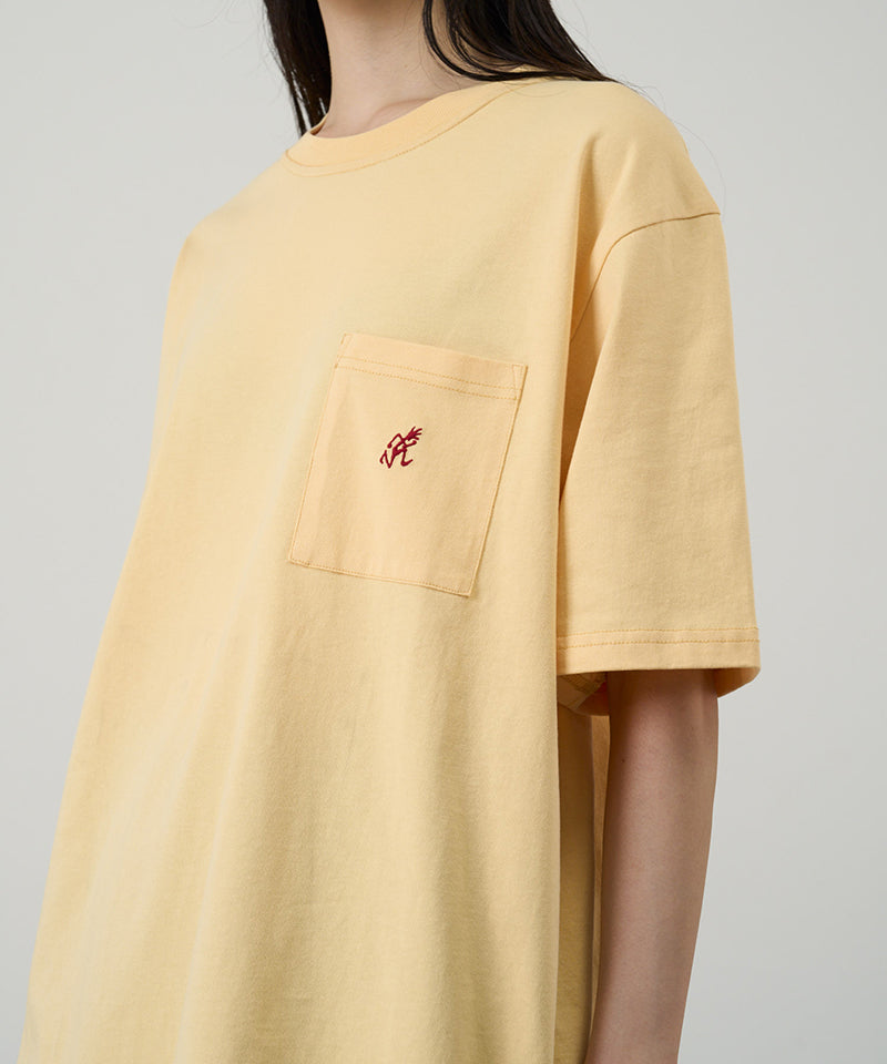Model wearing a Gramicci mango colored One Point Tee with a small running man graphic against a light-tone background.