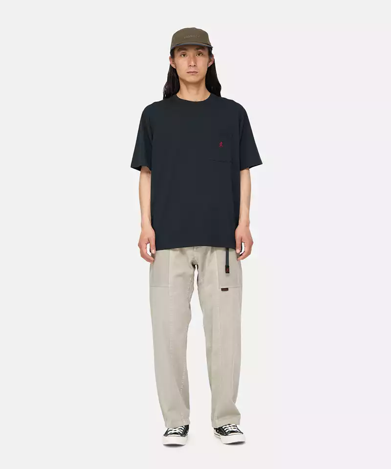 Model wearing a vintage black Gramicci One Point Tee with a small running man graphic and beige pants on a light-tone background.