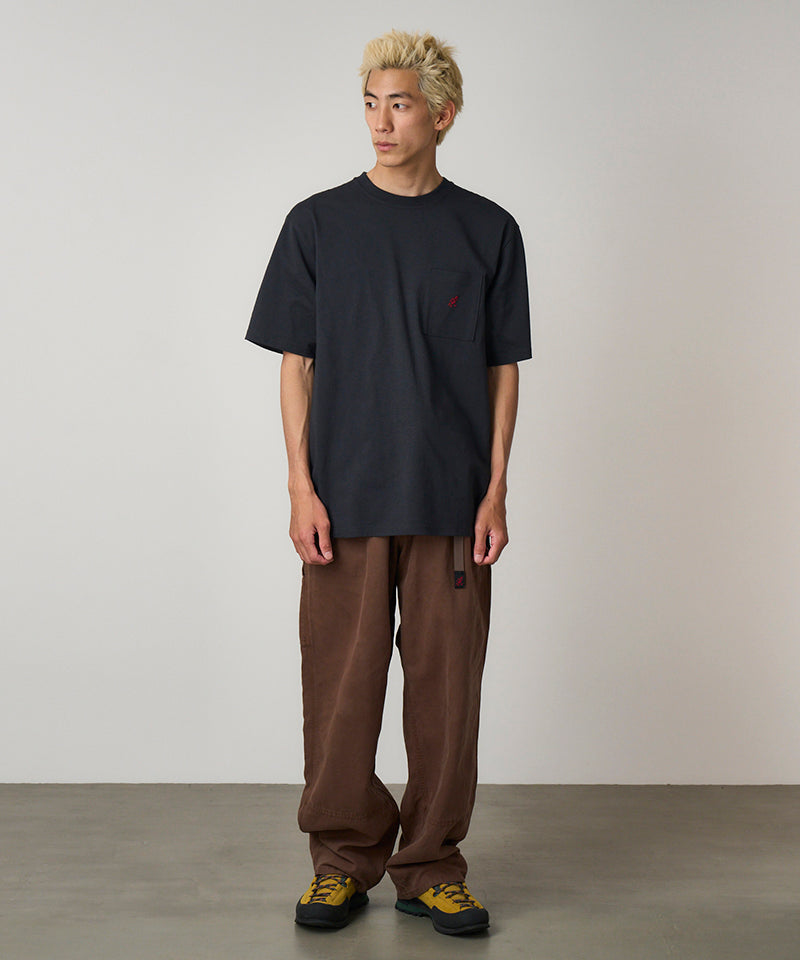 Model wearing a vintage black Gramicci One Point Tee with a small running man graphic and brown pants on a light-tone background.