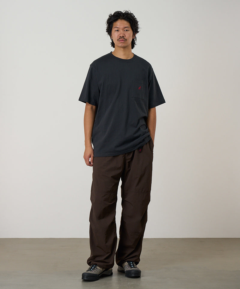 Model wearing a vintage black Gramicci One Point Tee with a small running man graphic and brown pants on a light-tone background.