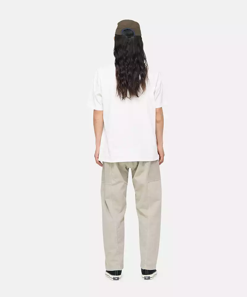 Back view of a model wearing a white Gramicci One Point Tee and beige pants on a light-tone background.
