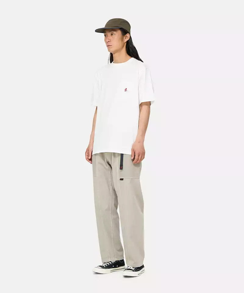 Model wearing a white Gramicci One Point Tee with a small running man graphic and beige pants on a light-tone background.