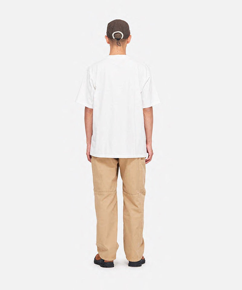 Back view of a model wearing a white Gramicci One Point Tee and khaki pants on a light-tone background.