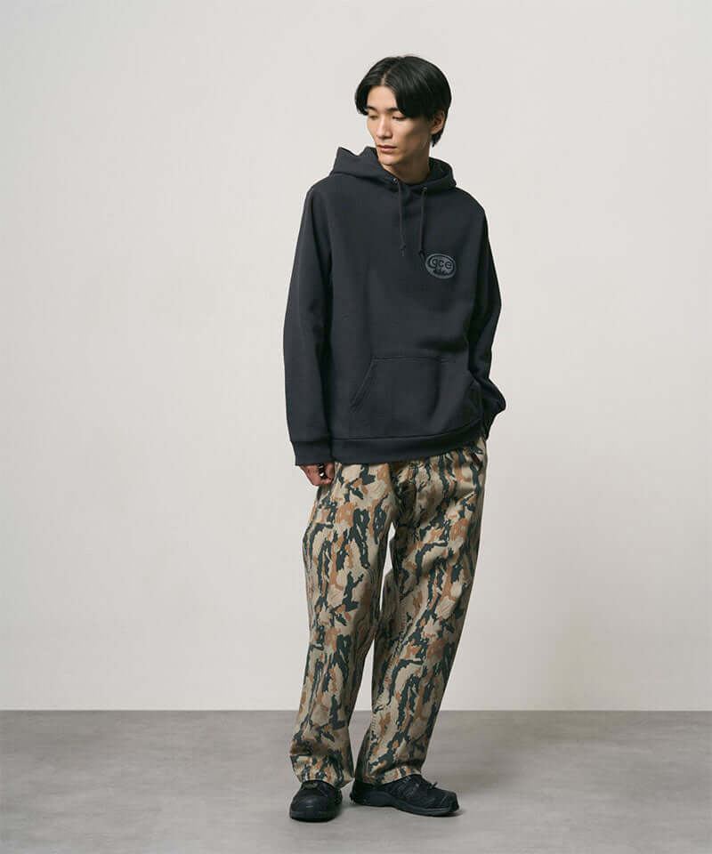 Model wearing bark camo Denim Gramicci Pant Straight Fit and a black hoodie on a light-tone background.