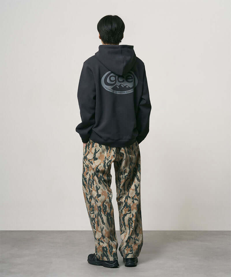 Back view of a model wearing bark camo Denim Gramicci Pant Straight Fit and a black hoodie on a light-tone background.