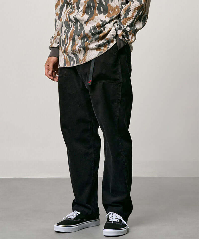Model wearing black Gramicci Corduroy Loose Tapered Ridge Pants and a camo shirt on a light-tone background.
