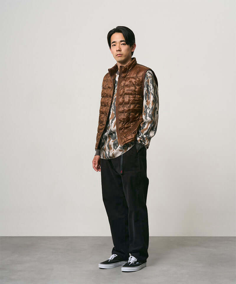 Model wearing black Gramicci Corduroy Loose Tapered Ridge Pants and a brown vest on a light-tone background.