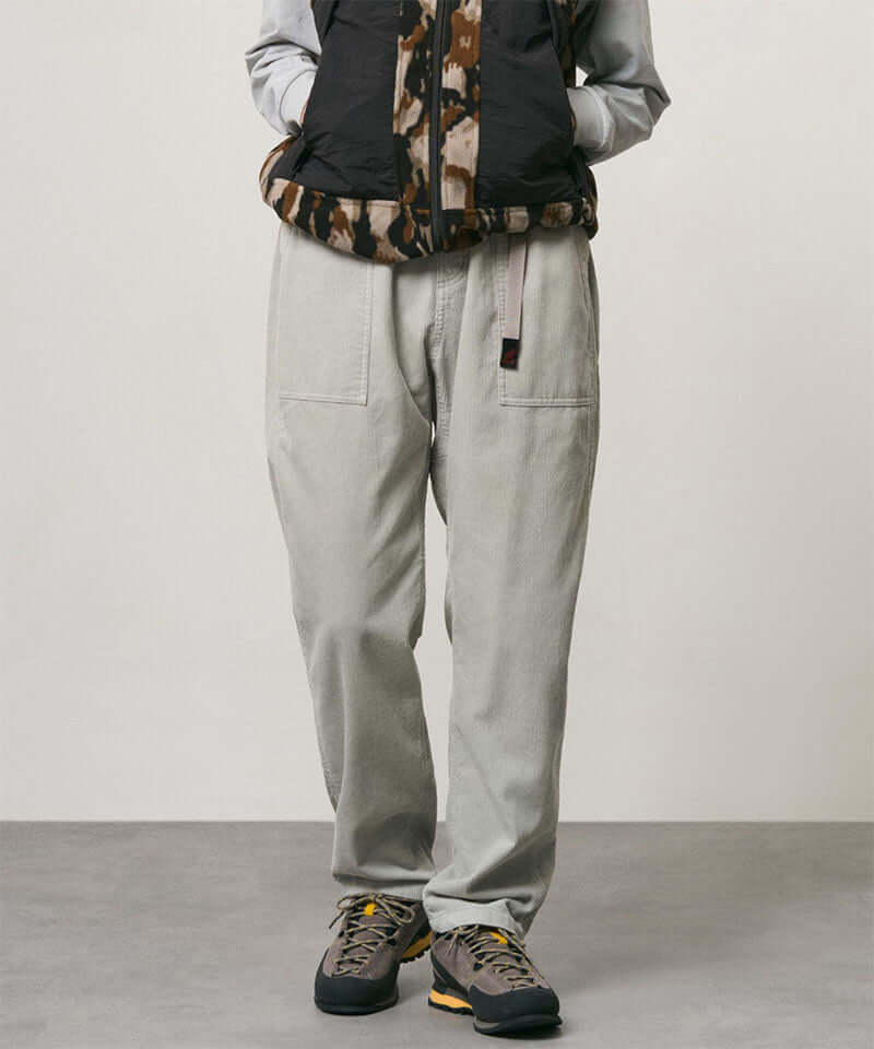 Model wearing smokey grey Gramicci Corduroy Loose Tapered Ridge Pants and a camo black jacket on a light-tone background.