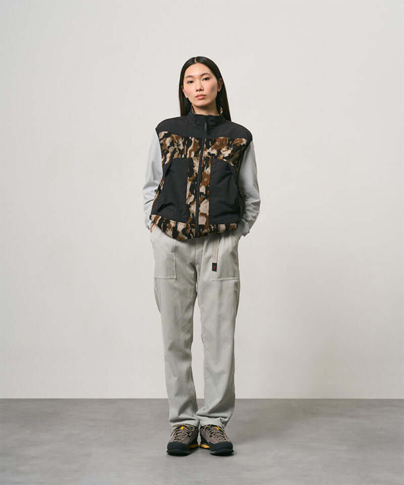 Model wearing smokey grey Gramicci Corduroy Loose Tapered Ridge Pants and a camo black jacket on a light-tone background.