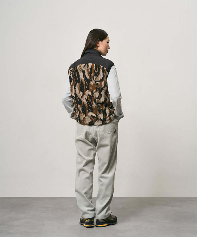 Back view of a model wearing smokey grey Gramicci Corduroy Loose Tapered Ridge Pants and a camo black jacket on a light-tone background.