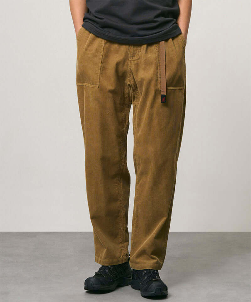 Model wearing tan Gramicci Corduroy Loose Tapered Ridge Pants and a black shirt on a light-tone background.