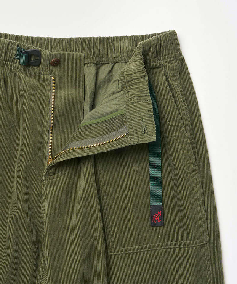 Close-up view of toned olive colored Gramicci Corduroy Loose Tapered Ridge Pants showing waistband and zipper detail on a light-tone background.