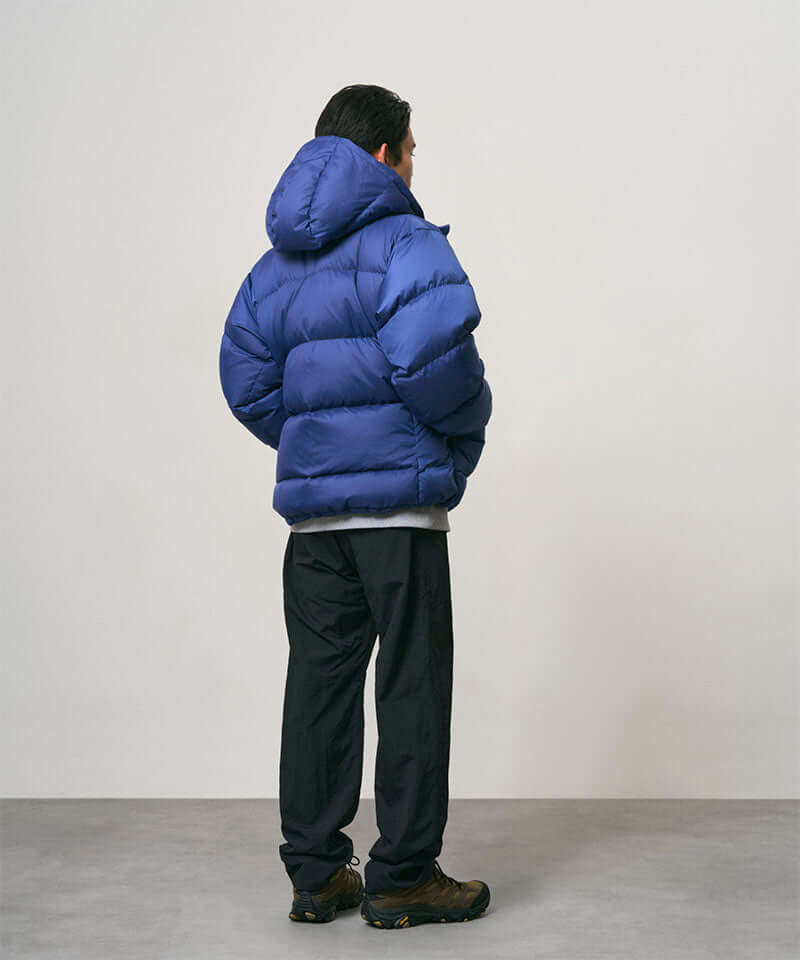 Back view of a model wearing black Nylon Gramicci Pants and a blue jacket on a light-tone background.