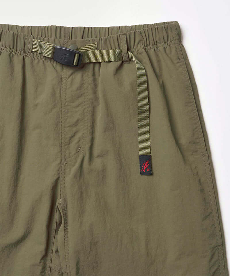 Close-up view of burnt olive colored Nylon Gramicci Pants on a light-tone background.