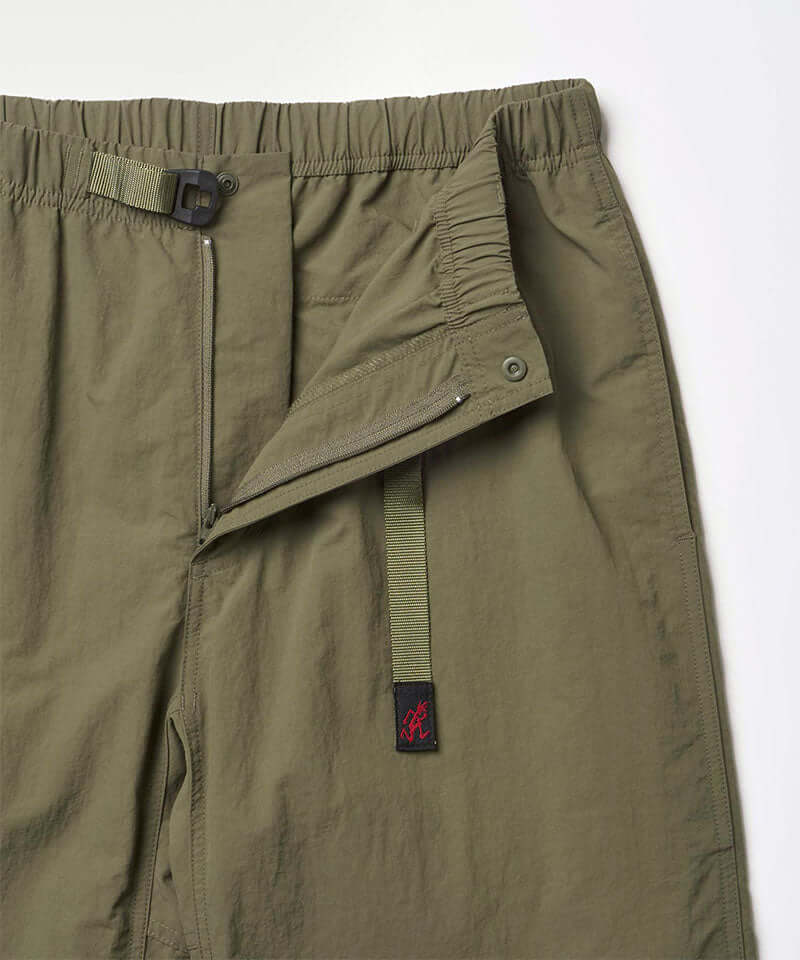 Close-up view of burnt olive colored Nylon Gramicci Pants showing waistband and zipper detail on a light-tone background.
