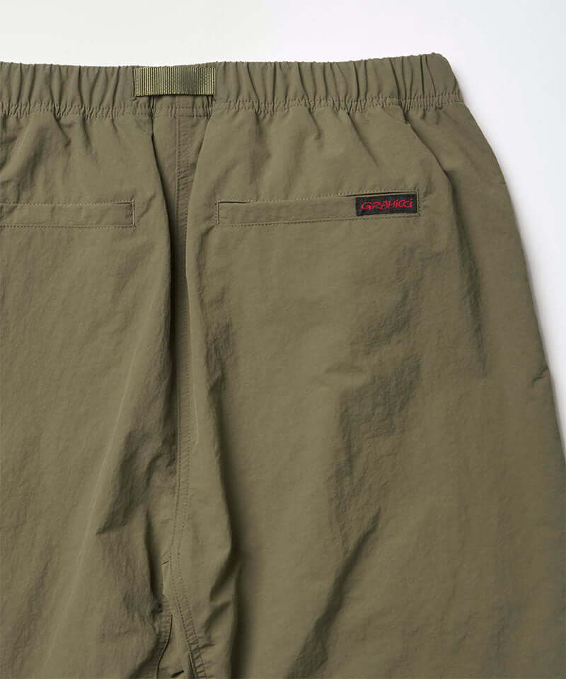 Close-up back view of burnt olive colored Nylon Gramicci Pants on a light-tone background.