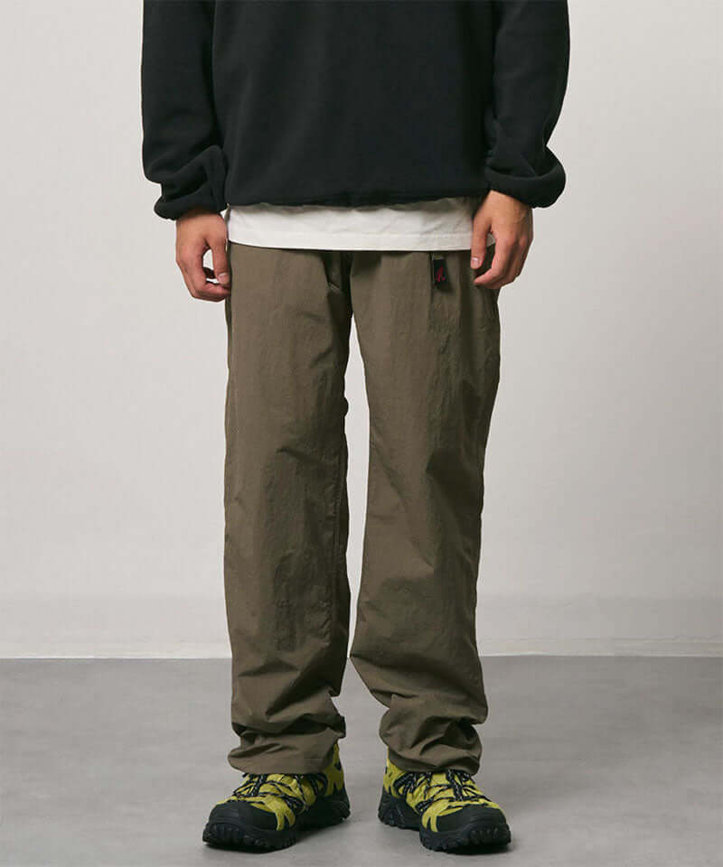 Burnt olive colored Nylon Gramicci Pants with a belt against a light-tone background.