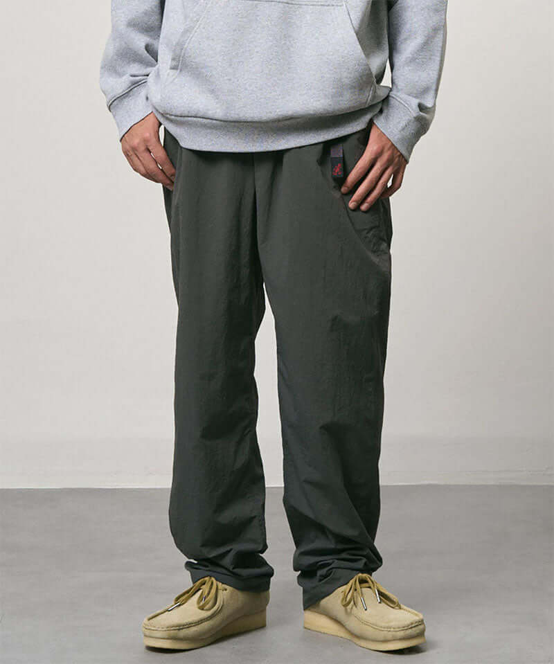 Model wearing carbon colored Nylon Gramicci Pants and a grey hoodie on a light-tone background.