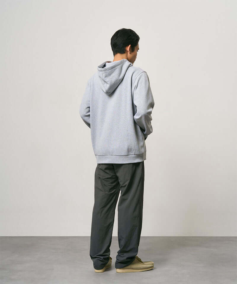 Back view of a model wearing carbon colored Nylon Gramicci Pants and a grey hoodie on a light-tone background.