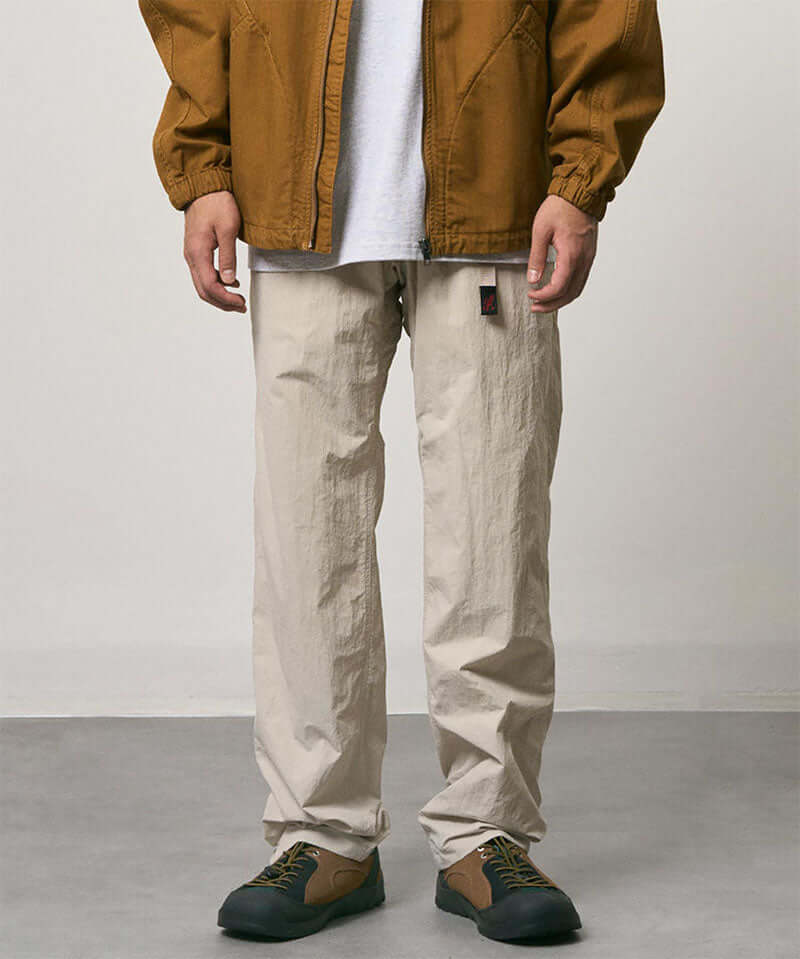 Model wearing stone colored Nylon Gramicci Pants and a brown jacket on a light-tone background.