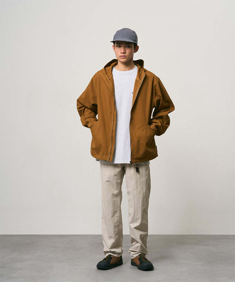 Model wearing stone colored Nylon Gramicci Pants and a brown jacket on a light-tone background.
