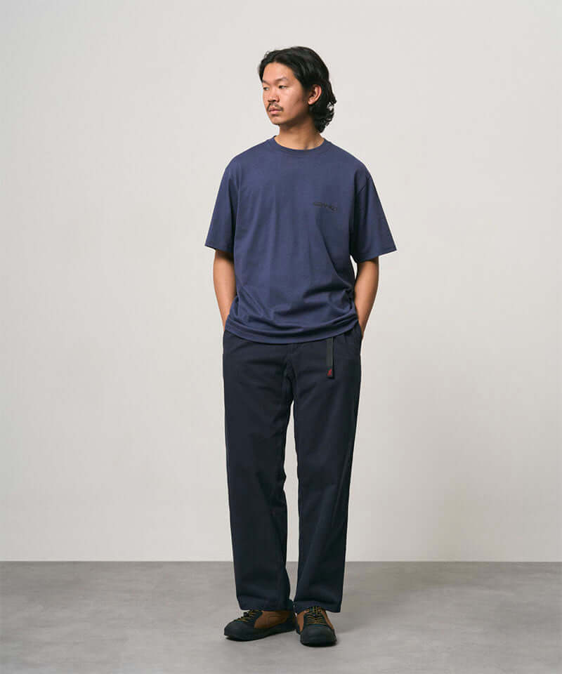 Model wearing a navy Gramicci Bass Tee and black pants on a light-tone background.