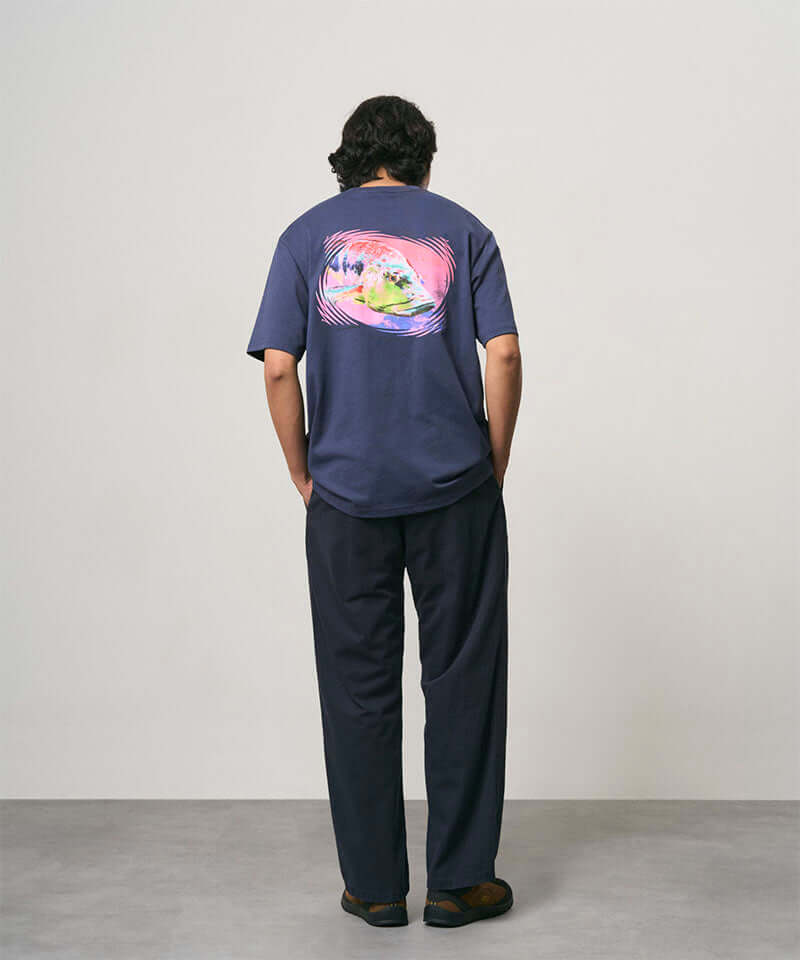 Model wearing a navy Gramicci Bass Tee and black pants on a light-tone background.