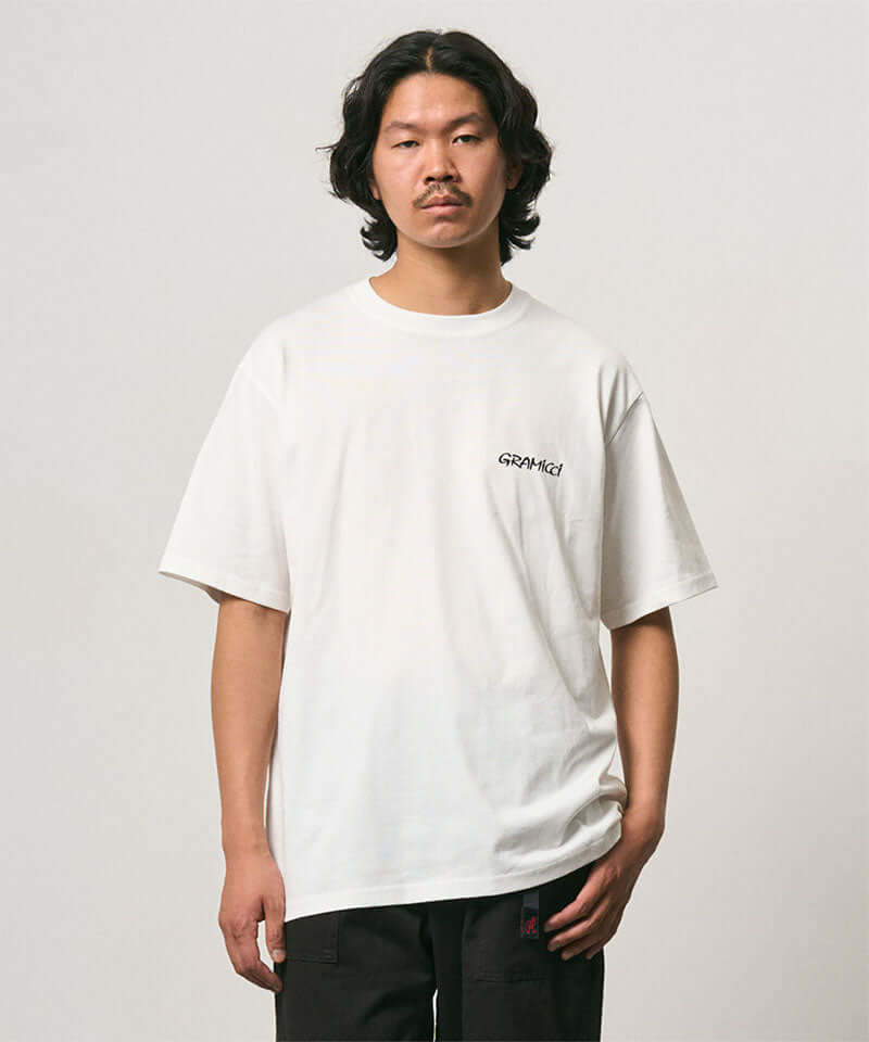 Model wearing a Gramicci white Bass Tee against a light-tone background.
