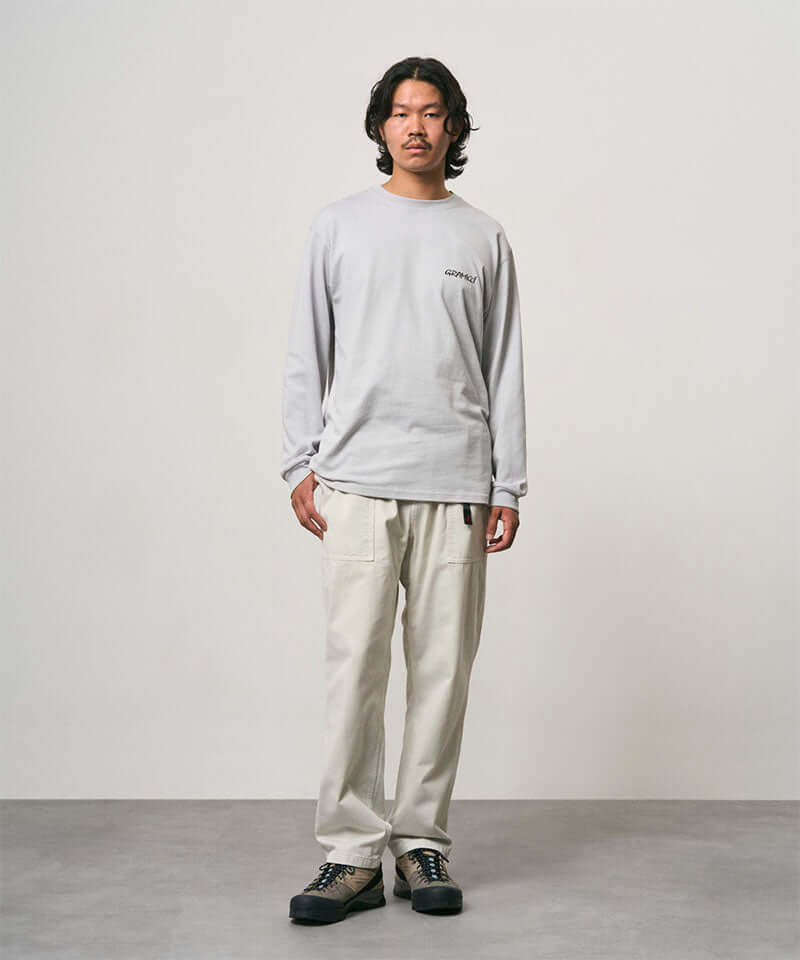 Model wearing a mist colored Gramicci Bass Long-Sleeve Tee and off-white pants on a light-tone background.
