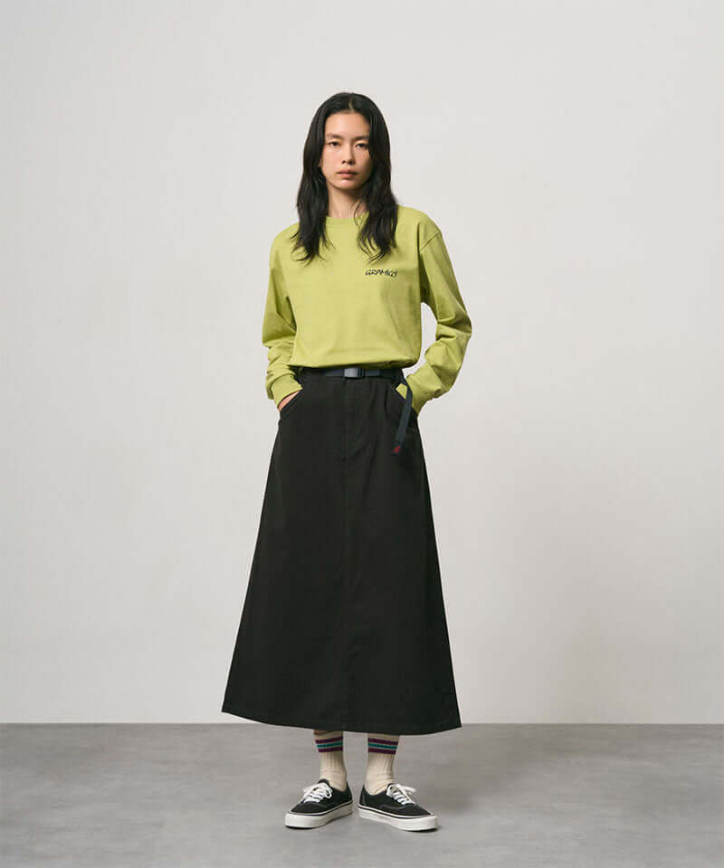 Model wearing a sweet pea colored Gramicci Bass Long-Sleeve Tee and black skirt on a light-tone background.