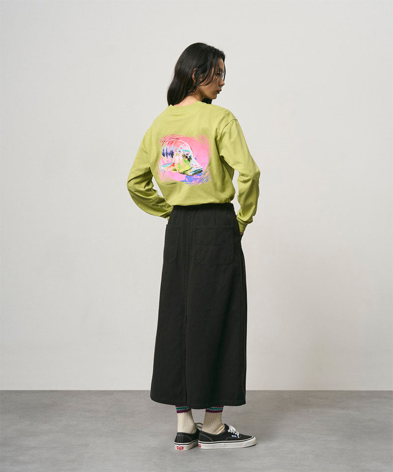 Back view of a model wearing a sweet pea colored Gramicci Bass Long-Sleeve Tee with a graphic and black skirt on a light-tone background.