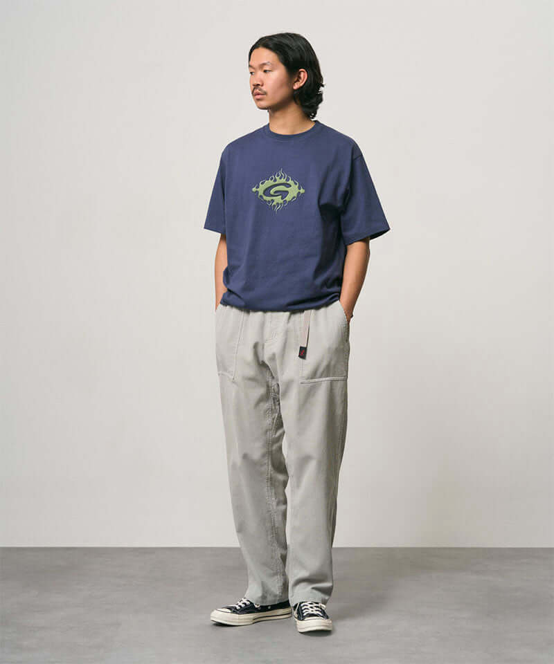 Model wearing a navy Gramicci Flames Tee with a graphic and light grey pants on a light-tone background.