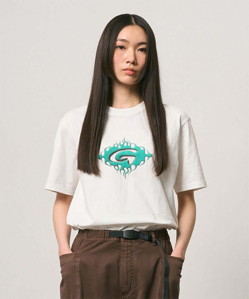 Model wearing a Gramicci white Flames Tee with a graphic against a light-tone background.