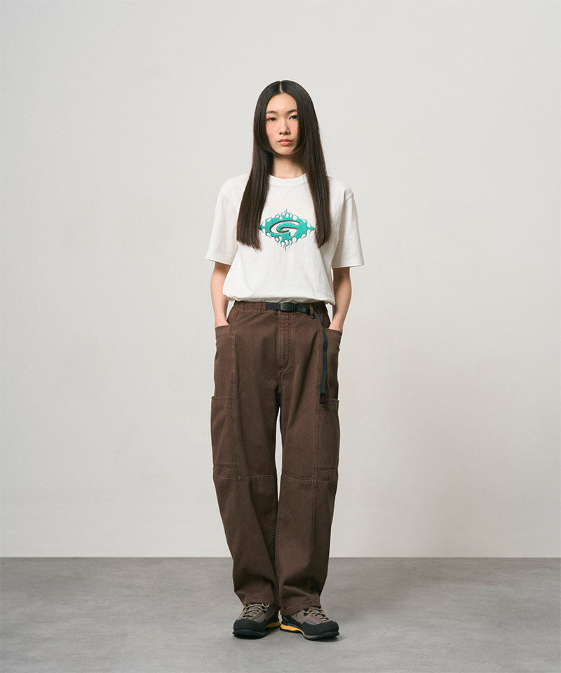 Model wearing a white Gramicci Flames Tee with a graphic and brown pants on a light-tone background.