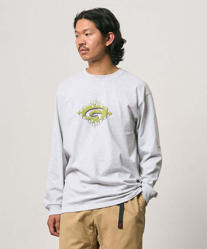 Model wearing a Gramicci ash heather colored Flames Long Sleeve Tee with a graphic against a light-tone background.