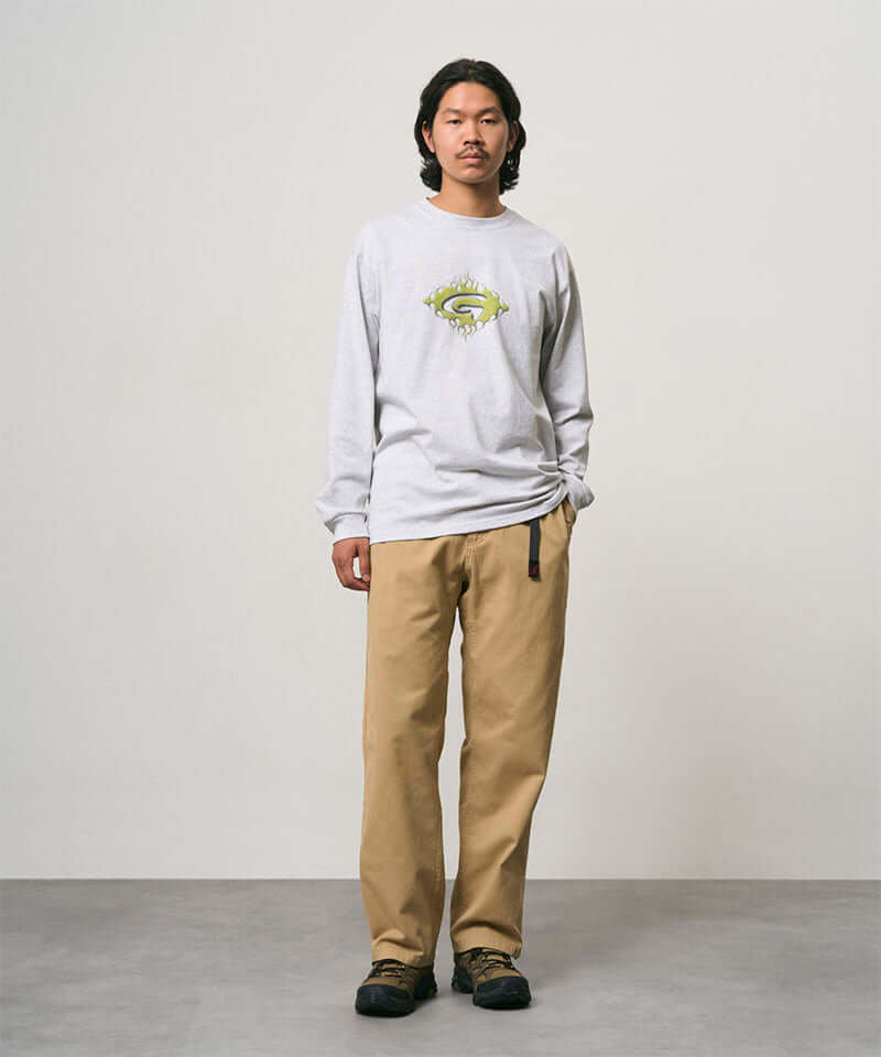 Model wearing a ash heather colored Gramicci Flames Long Sleeve Tee with a graphic and beige pants on a light-tone background.