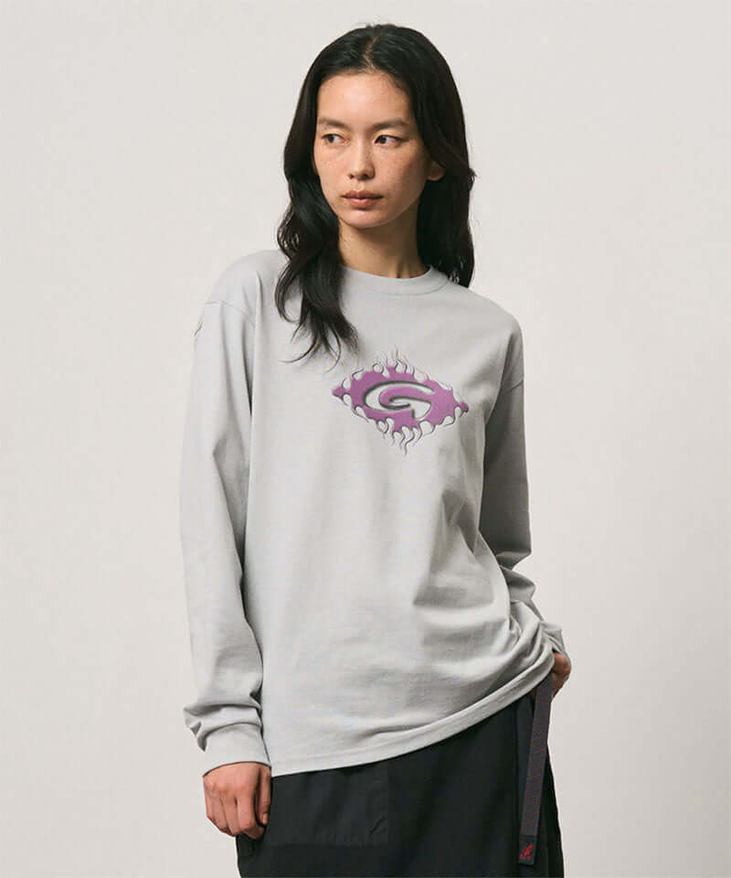 Model wearing a Gramicci mist colored Flames Long Sleeve Tee with a graphic against a light-tone background.