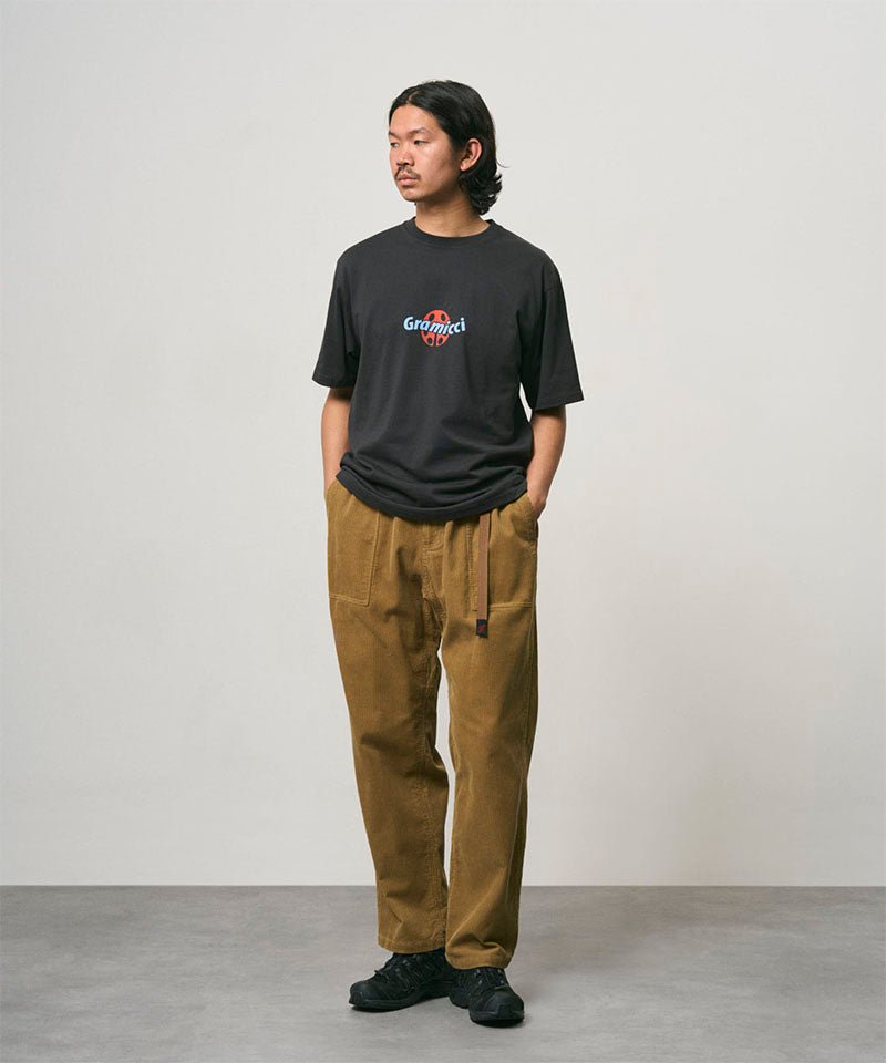 Model wearing a vintage black Gramicci Ladybug Tee with colorful graphic and brown pants on a light-tone background.